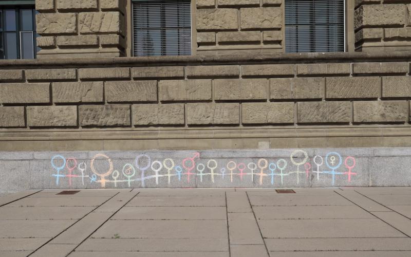 Brick exterior wall of building with multi-coloured chalk drawings of female and male symbols.